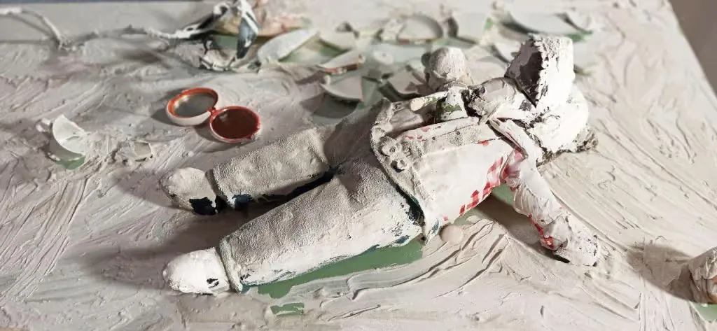Plaster-covered doll lying among ceramic shards on Pamela Mattana's white door installation