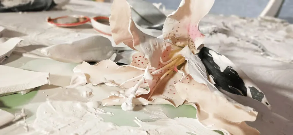 Close-up of a ceramic lily among plaster and broken pieces on Pamela Mattana's door installation