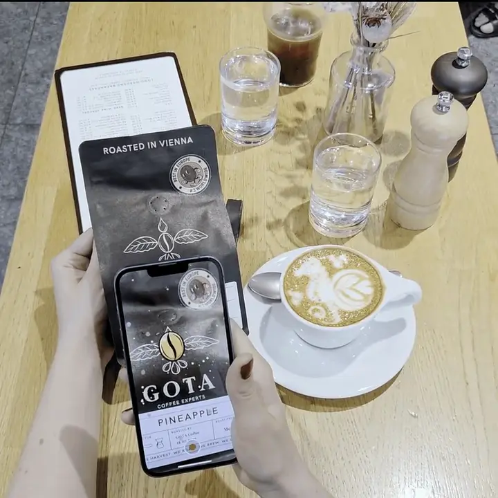 A phone held over a Gota Coffee bag on a café table: the packaging comes alive on the screen