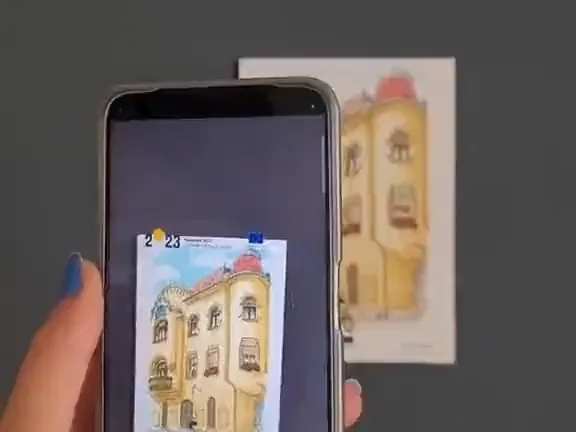 A postcard of a drawn Timisoara facade held in the hand, its windows lighting up in AR